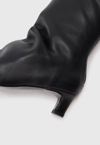 Bottine en cuir noir au design lâche, avec un bout pointu et un petit talon carré. La texture semble lisse avec de subtils plis.