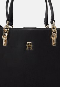 Sac à main en cuir noir avec chaîne dorée et doubles poignées, avec un petit logo TH doré entrelacé à l'avant.