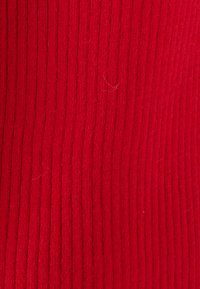 Tessuto rosso a righe verticali, morbido al tatto e leggermente peloso, che indica calore e una possibile costruzione a maglia.