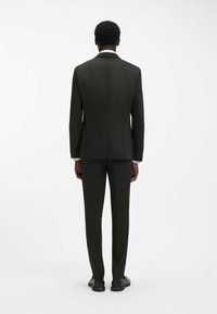 Completo verde scuro su misura, giacca monopetto e pantaloni abbinati. Tessuto liscio con leggero lucido, dettaglio cucitura posteriore e design minimalista.