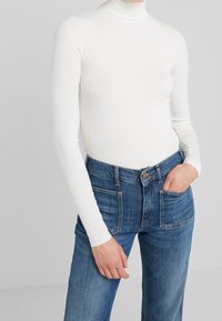 Vit ribbad långärmad polotröja kombinerad med blå högmidjade jeans med framfickor och en lätt blekning.