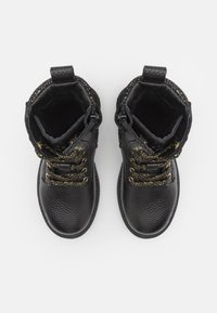 Černé kožené kotníkové boty s texturovaným povrchem, zlatými šňůrkami a dekorativními perforacemi kolem horního okraje. Plochá, odolná podrážka.