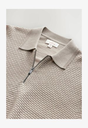 Pull-over en tricot beige avec un motif structuré et texturé, un col court, et une fermeture éclair d'un quart de longueur avec tirette noire.