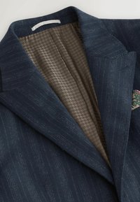 Tengerészkék blézer finom csíkos mintával, mintás barna béléssel és színes zsebkendővel. Figyelemre méltó hajtókájú dizájn.