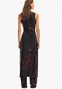 Czarna sukienka bez rękawów z kwiatowym wzorem w odcieniach czerwieni, złota i czerni; dopasowana sylwetka prowadząca do rozkloszowanego dołu.
