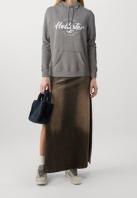 Sudadera gris con logotipo blanco, falda maxi de mezclilla marrón, bolso peludo azul marino y zapatillas gris con rayas claras. Texturas suaves, estilo casual.