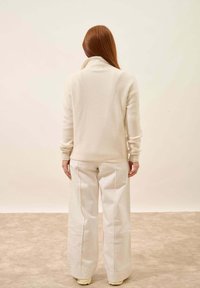 Biały sweter o prążkowanej strukturze z wysokim kołnierzem, w zestawieniu z szerokimi białymi spodniami. Zestaw charakteryzuje się miękką teksturą i minimalistycznym wzornictwem.