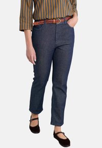 Tamno plavi traper ravni hlače s prednjim džepovima, uparen s pletenim smeškim kožnim pojasom i tamno smeškim balerinama. Prugasta višebojna majica.