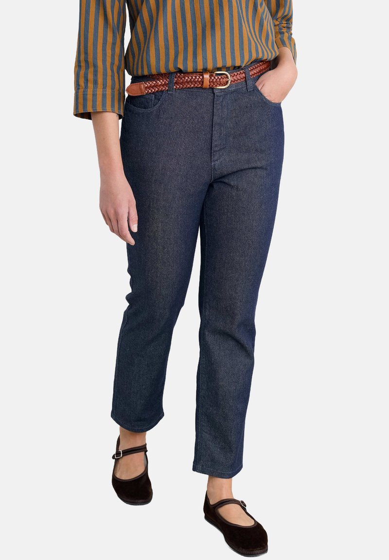 Tumedat sinise denimi sirgedega püksid ees olevate taskutega, kaunistatud punutud pruuni nahkvööga ja tumedate pruunide lamedaontidega. Triibuline mitmevärviline särk.