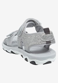 Silver glittrande sandaler med justerbara remmar, vadderad grå sula och strukturerat svart mönster. Öppen design för andningsförmåga och komfort.