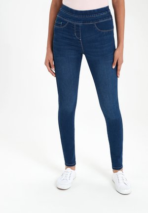 Leggings en denim bleu foncé taille haute avec une finition lisse. Comprend une poche avant et des coutures contrastées. Associés à des baskets blanches.