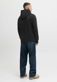 Zwarte hoodie met een gestructureerde afwerking, voorzien van een verstelbare capuchon. Gecombineerd met losse blauwe denim jeans en beige schoeisel.