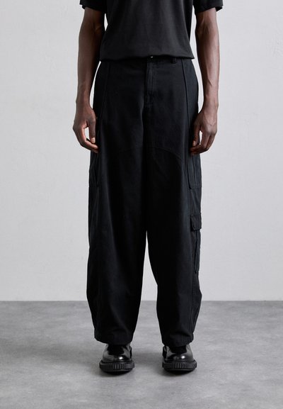 Pantalons cargo noirs à coupe décontractée, avec taille ajustable, poches latérales et texture de tissu lisse, assortis à des chaussures noires.