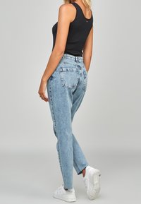 Černý žebrovaný top na ramínka, světle modré džíny vysokého pasu s jemným blednutím a bílé tenisky; na zadní kapse je vyšitý akcent.