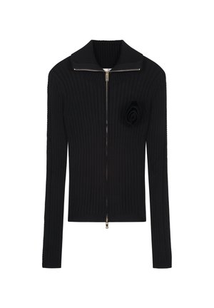 Zwarte geribbelde gebreide cardigan met een brede kraag, ritssluiting aan de voorkant en een stoffen rozenaccent aan de linkerkant. Lange mouwen en een aansluitend design.