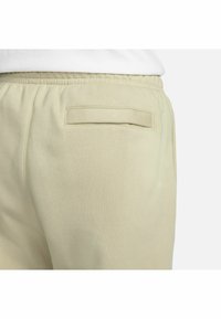 Lichtbeige trainingsbroek met een gladde textuur, elastische tailleband en een enkele achterzak met een gevouwen klepdetail.