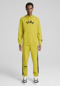 Gul huvtröja med svart text, kombinerad med matchande gula joggers med svarta sidostreck och svart logotyp. Komposit design för sportkläder.