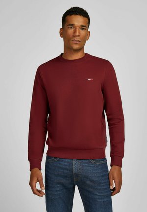 Sweat à col rond bordeaux avec des manches longues. Présente un petit logo sur la poitrine et des poignets et un ourlet côtelés.