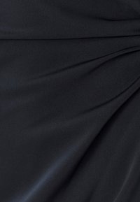 Juoda audinio medžiaga su lygiu paviršiumi, pasižymi švelniais klostais ir raukšlėmis, kurios sukuria subtilų blizgesį visame paviršiuje.