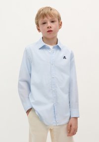 Camicia button-up azzurra con maniche lunghe, caratterizzata da un ricamo nero di teschio e ossa incrociate sulla parte sinistra del petto. Tessuto di cotone liscio.