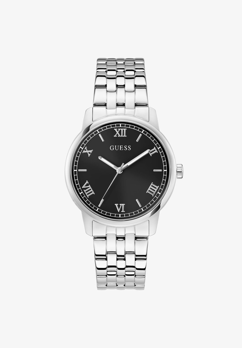 Montre-bracelet en métal argenté avec cadran noir, chiffres romains, trois aiguilles, et le nom de la marque GUESS au centre.