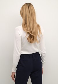 Bluza albă cu mâneci lungi, cu un decolteu rotund, combinată cu pantaloni bleumarin. Textură fină, stil mulat și talie cu elastic.