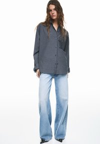 Kockovaná košeľa na zapínanie na gombíky v námorníckej modrej a bielej farbe, doplnená svetlomodrými širokými džínsami. Obe položky majú voľný strih a hladkú textúru látky.