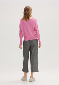 Pull côtelé rose à coupe ample avec épaules tombantes, associé à un pantalon court à carreaux gris et des baskets blanches à lacets.