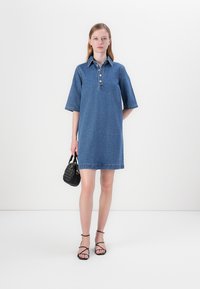 Denim skjortekjole med knappestolpe, korte ermer og rett silhuett. Brukt med en liten svart håndveske og sandaler med stropper.