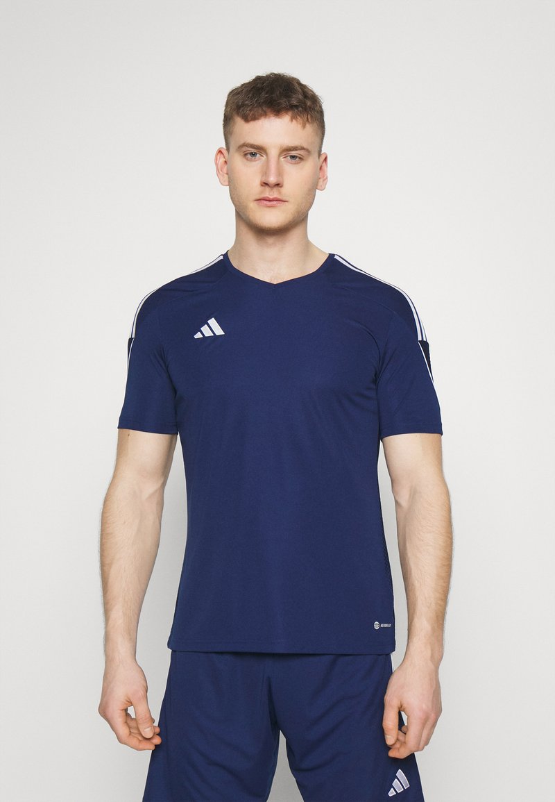 Camiseta atlética azul marino de manga corta, con diseño de cuello en V y acentos blancos en los hombros. Fabricada con un tejido suave y transpirable.