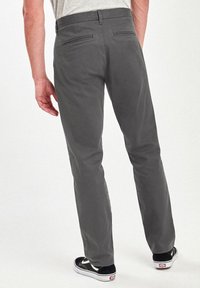 Pantalons gris à coupe droite, dotés de deux poches arrière et d'une texture lisse. Associés à des baskets noires et un haut gris.
