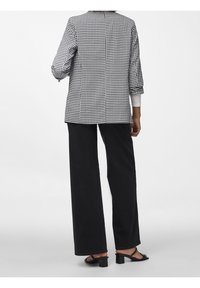 Blazer en blanco y negro de cuadros con un silueta recta, mangas de tres cuartos y abertura trasera. Lleva puesto sobre pantalones anchos negros y sandalias.