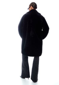 Čierny umelý kožušinový kabát so širokým golierom, mierne voľným strihom a dlhými rukávmi. Kombinovaný s tmavými rozšírenými džínsami, ktoré majú hladkú textúru.