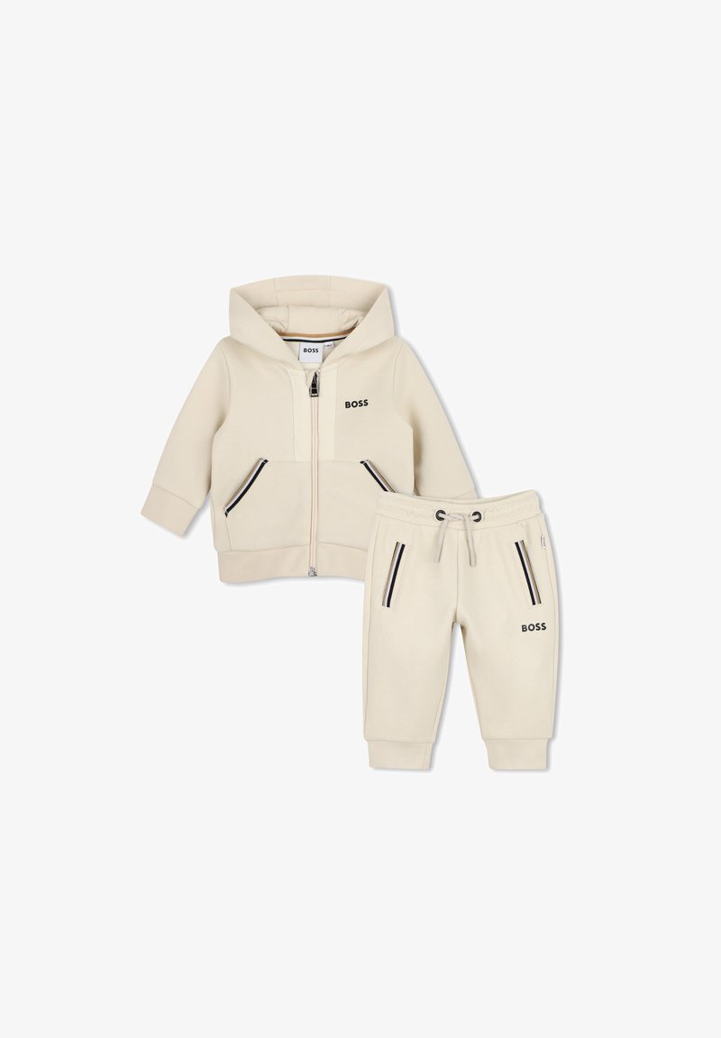Sweat à capuche pour tout-petit couleur crème avec joggings assortis, fermeture éclair à l'avant et poches, marqué "BOSS" sur la poitrine et la jambe.