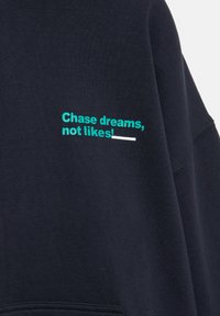 Tengerészkék pulóver zöld "Chase dreams, not likes!" felirattal hímzett az elején. Puha anyag, laza kialakítás.