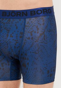 Zilā bokseršortos ar melnu abstraktu rakstu, kam ir melnais elastīgais jostasvērts ar uzrakstu "BJÖRN BORG". Mīksta auduma, pieguļošs dizains.