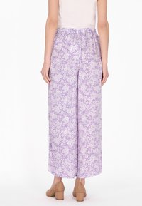 Lichtpaarse wijde broek met een witte bloemenpatroon, uitgerust met een elastische tailleband. Ggedragen met bruine blokhak schoenen.