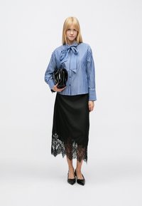 Blauw-wit gestreepte blouse met strik, gecombineerd met een zwarte satijnen rok met een kanten zoom, en zwarte puntige platte schoenen.