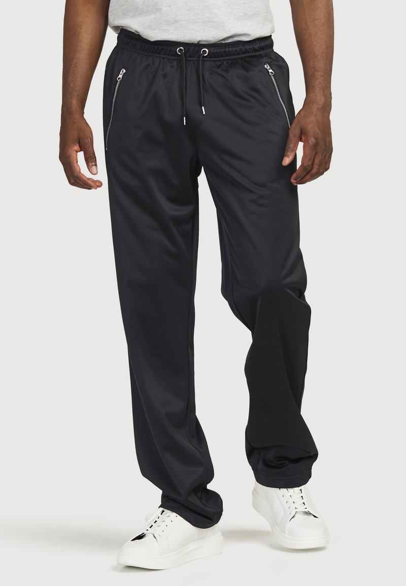 Schwarze Sporthose mit lockerer Passform, ausgestattet mit einem Kordelzug am Bund und Reißverschlusstaschen an den Seiten, aus glattem, leichtem Material.