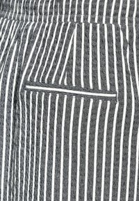 Schwarz-weiß gestreifter Stoff mit einem strukturierten Muster, einem kleinen, eingesetzten Taschen und einer glatten Naht entlang der Kante.