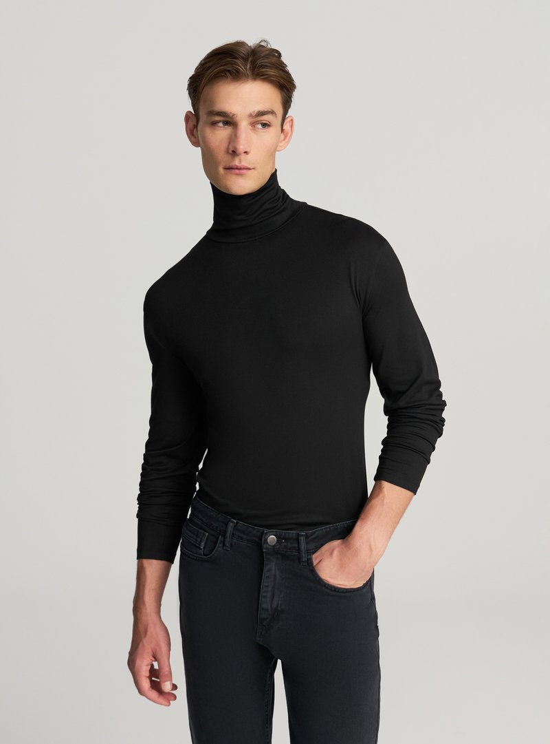 Dolcevita nero in tessuto elasticizzato, design aderente con maniche lunghe, texture liscia, abbinato a jeans scuri. Nessun motivo o accento visibile.