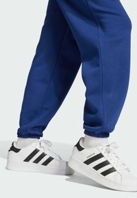 Vita sportskor med svarta ränder, kombinerade med blåa träningsbyxor med elastiska muddar. Skorna har en texturerad sula och vadderad krage.