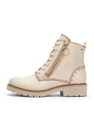 Botas de tobillo beige de cuero, con cremallera frontal, diseño con cordones, detalles de tachuelas en el tacón y suela de bloque.