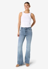 Φαρδιά τζιν σε ανοιχτό μπλε χρώμα από τζιν ύφασμα, συνδυασμένα με λευκό ριμπ τοπ χωρίς μανίκια. Τα τζιν διαθέτουν κλασικό σχέδιο με πέντε τσέπες και κλείσιμο με κουμπί.