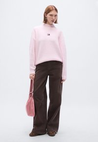 Pulover roz cu model în dungi și guler înalt, pantaloni maro cu picioare largi și geantă roz de umăr. Pantofi loafer cu model completează ținuta.