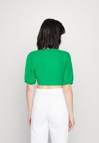 Top court vert avec manches bouffantes courtes, tissu texturé et ourlet festonné. Porté avec un jean blanc taille haute.