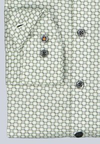 Langarmhemdmanschette mit grün-weißer geometrischer Kreisgestaltung und dunklen Knöpfen, eine Naht des Knopfes ist mit orangefarbenem Faden genäht.