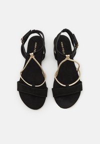 Black suede sandals featuring a gold metallic strap design with a cross pattern and an ankle strap for secure fit. Low heel style.