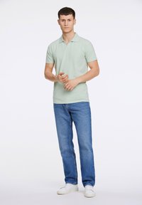 Ljust grön pikétröja med krage, korta ärmar, tillsammans med raka blåjeans och vita sneakers. Enkel och minimalistisk design.