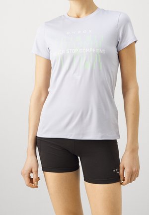 Personne portant un t-shirt gris clair Puma HYROX à manches courtes avec le texte "Never Stop Competing" et un short ajusté noir HYROX.